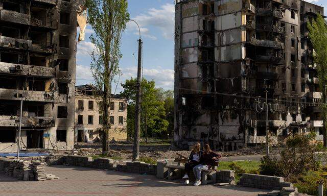 Zwei ukranische Frauen sitzen in Borodjanka vor zerstörten Wohnhäusern.
