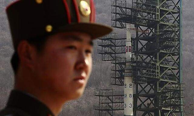 A soldier stands guard in front of the Unha-3 (Milky Way 3) rocket sitting on a launch pad at the Wes