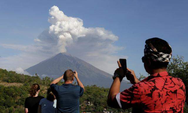 A local guide and foreign tourists take pictures of Mount Agung volcano erupting from Amed, Karangasem Regency in Bali