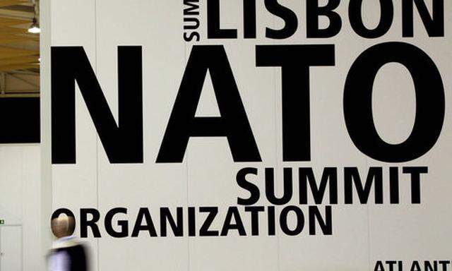A man walks by a logo printed on a wall inside the NATO summit venue in Lisbon, Portugal on Thursday,