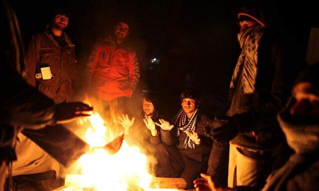 Migrants warm up around a fire at camp 'Lipa' after it was closed, in Bihac