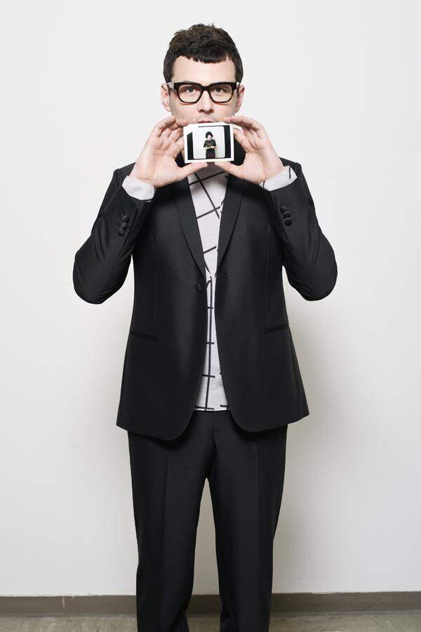 Manuel Rubey hält ein Polaroid in die Kamera, auf dem die Regisseurin Marie Kreutzer zu sehen ist. Er trägt auf diesem Foto einen Anzug und einen Pullover von Emporio Armani.