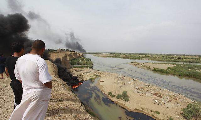 Residents look on as oil leaks into the Tigris River while smoke rises in Tikrit