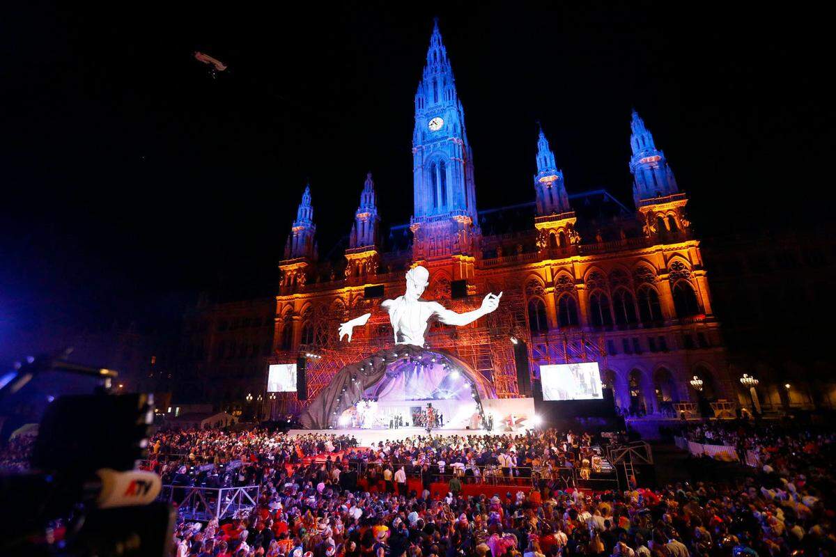 Der Star des Abends war, nun ja, überlebensgroß. Jener Conférencier, der schon seit Tagen vor dem Wiener Rathaus wachte, wurde am Samstagabend beim Life Ball spektakulär mit modernster Projektionstechnik zum Leben erweckt. Wer sich an Robert Dornhelms St. Margarethener „Tosca“-Engel von 2015 erinnert fühlte, lag nicht falsch: Amra Bergmann hat da wie dort das Bühnenbild geschaffen. Wie schon damals wurde der Raum unterhalb der Figur zur sich wandelnden Kuppel, in der das Geschehen unter der Regie von Giorgio Madia über die Bühne ging. In diesem Fall: eine Revue. Text: von Teresa Schaur-Wünsch und Köksal Baltaci