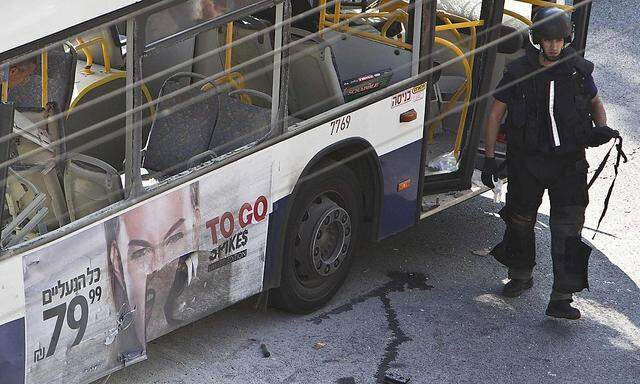 An Israeli police explosives expert walks next to a damaged bus at the scene of an explosion in Tel Aviv