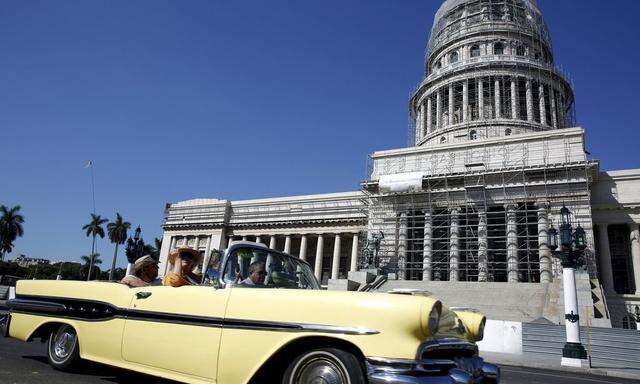 Tourists ride in a vintage car past the Capitol building which is undergoing restauration works in Havana