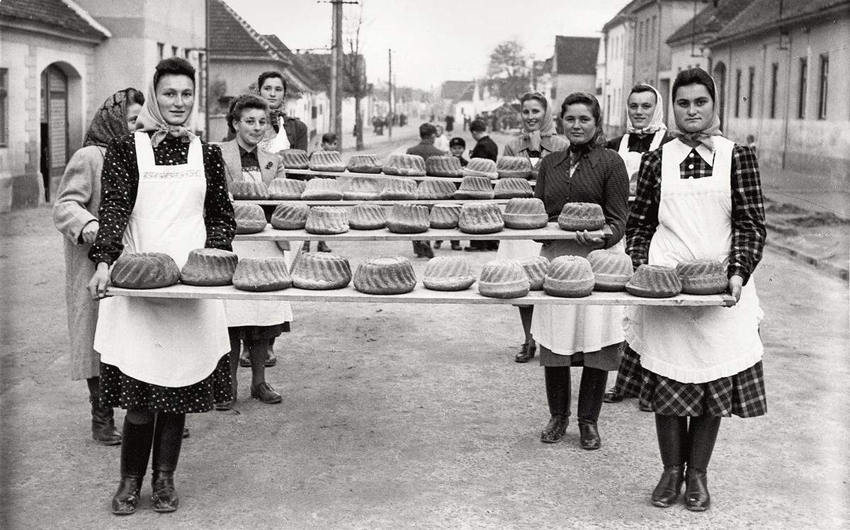 Frauen tragen in Mörbisch 150 Gugelhupfe in drei Partien zur Hochzeitstafel. Gruppenbild in der Hauptstraße, um 1950.