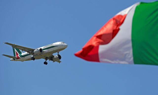 An Italy flag flutters as an Alitalia airplane approaches to land at Fiumicino airport in Rome