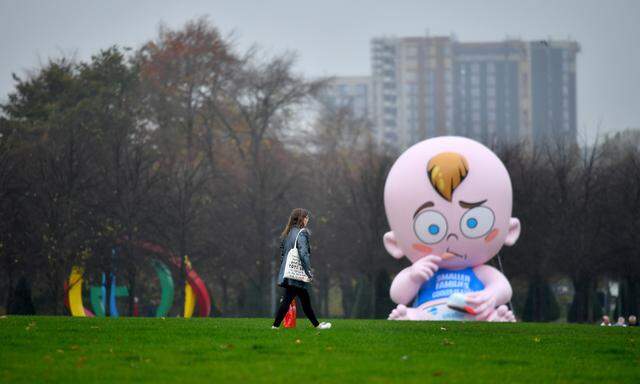 A woman walks past a giant baby balloon inflated by Climate Change activists in the rain at Glasgow Green as the UN Climate Change Conference (COP26) takes place, in Glasgow