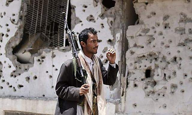 A tribal fighter loyal to Sadiq al-Ahmar, the leader of the Hashed tribe, walks in front of a bullet-