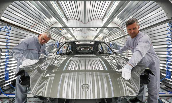 Zwei Porsche-Mitarbeiter prüfen in der Lackiererei den Lack der Karosserie eines vollelektrischen Porsche Macan im Werk Leipzig.