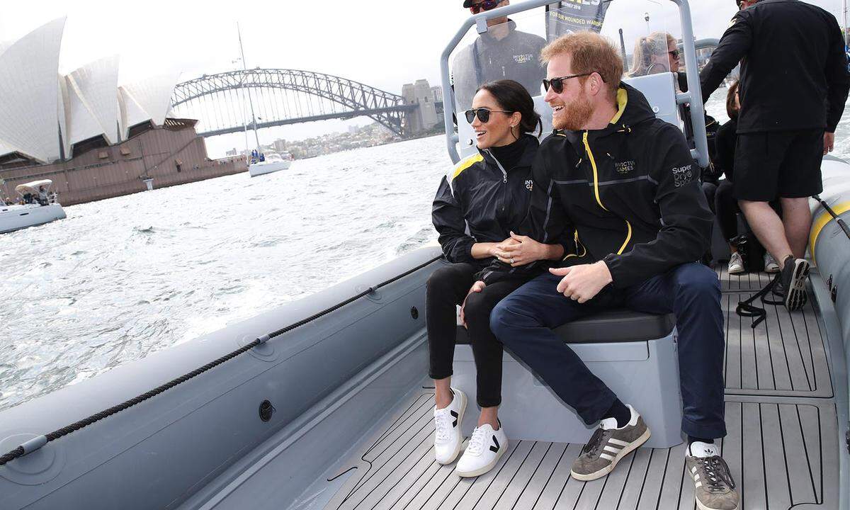 Im Wettkampfmodus: Prinz Harry und seine Frau bestaunten die Segelwettkämpfe im Hafen von Sydney. Wir bestaunen ihr praktisch-sportives Outfit: Ihren Look vom Vormittag wandelte sie nur minimal um. Statt Blazer und Pumps gibt es eine Wind-und-Wetter-Jacke der Invictus Games und weiße „V10 Extra White Black“-Sneaker von Veja um erschwingliche 125 Euro. Ein echter Hingucker ist die „Gravier“-Sonnenbrille von Krewe.