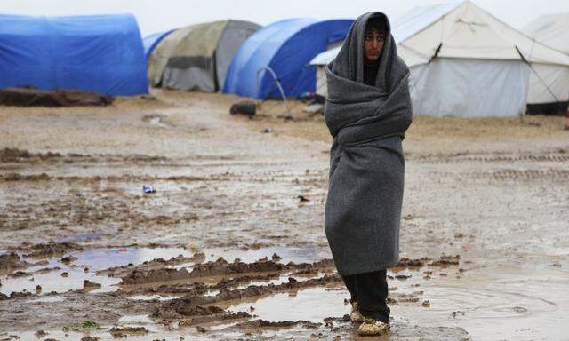 A refugee from the minority Yazidi sect wraps himself with a blanket as he stands on a muddy path during wintry weather at Nowruz refugee camp in Qamishli