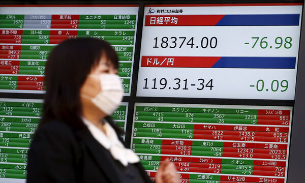 A woman walks past a screen displaying market data and exchange rates between the Japanese yen and the U.S. dollar outside a brokerage in Tokyo