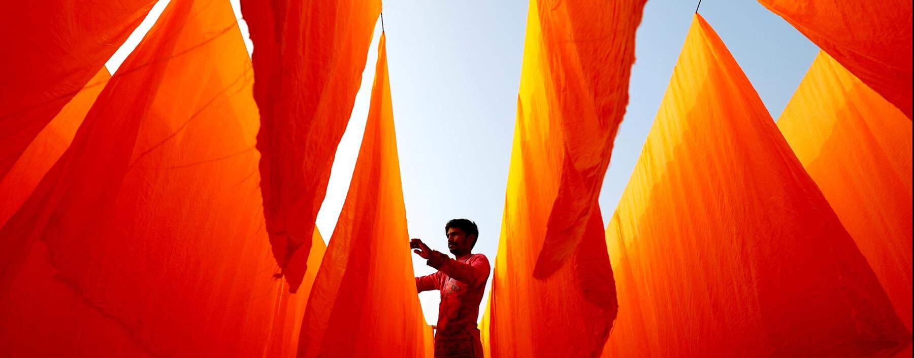 Ein Textilarbeiter in Bangladesch hängt Stoffe zum Trocknen auf, nachdem diese eingefärbt wurden.