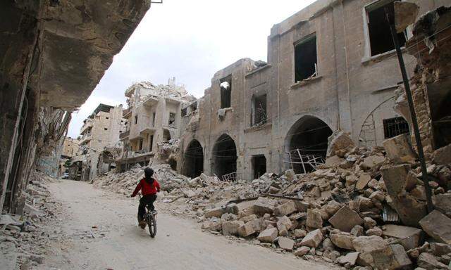 A boy rides a bicycle near damaged buildings in the rebel held area of Old Aleppo