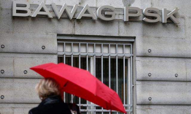 FILE PHOTO: A woman holding an umbrella passes the headquarters of Austrian lender BAWAG PSK in Vienna