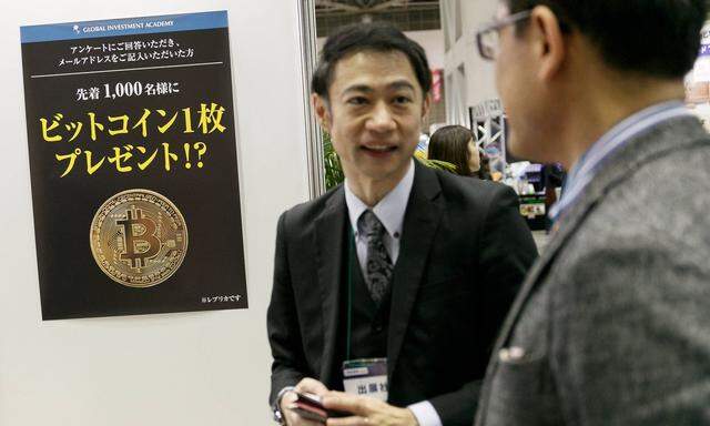 An exhibitor speaks about cryptocurrency Bitcoin to a visitor during the 1st Asset Management Expo o