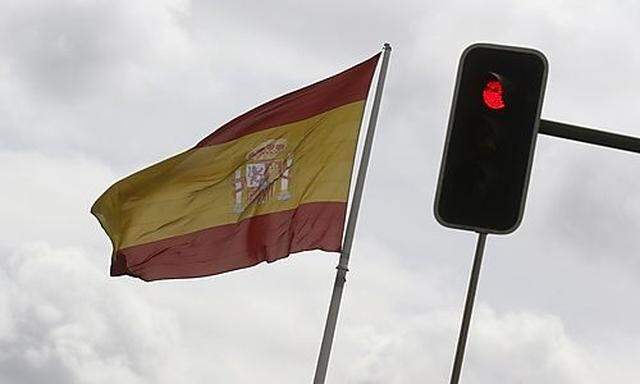 A Spanish national flag flies near a red traffic light in central Madrid