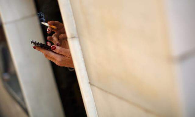 Woman smokes a cigarette as she holds a smartphone in the Andalusian capital of Seville