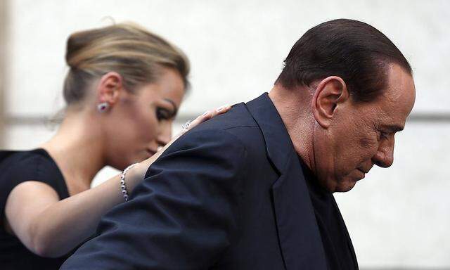 Former Italian Prime Minister Silvio Berlusconi leaves the stage flanked by his girlfriend Francesca Pascale at the end of a rally to protest his tax fraud conviction, outside his palace in central Rome