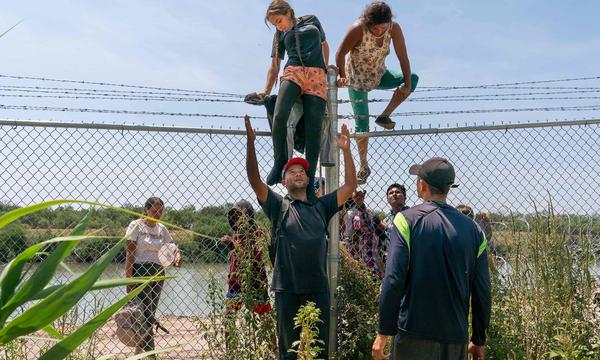 Menschen versuchen von Mexiko über einen Stacheldrahtzaun in die USA zu klettern.