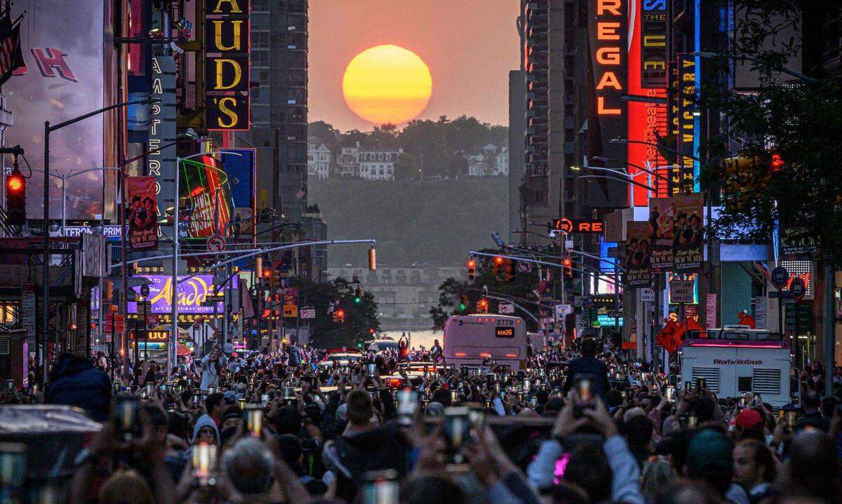 1. Juni. Das sogenannte Manhattanhenge wird in New York City von vielen Schaulustigen boabachtet und am Handy festgehalten. Der Sonne steht nur an wenigen Tagen parallel zu den Ost-West-ausgerichteten Straßen.