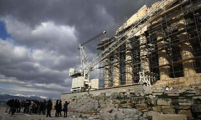 Tourists look at the temple of Parthenon atop the Acropolis hill in Athens