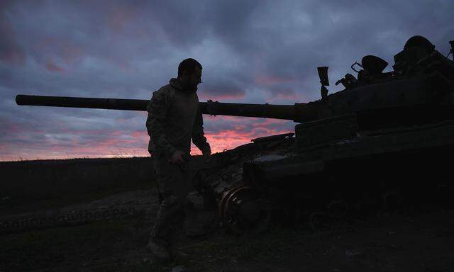 Ein ukrainischer Soldat geht bei Sonnenuntergang in der Nähe von Izium in der Nähe eines zerstörten Panzers spazieren