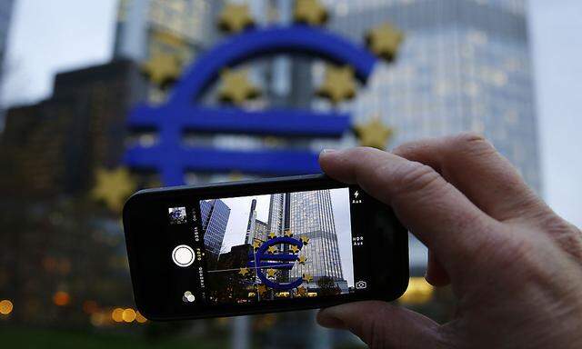 A man uses his mobile phone to take a picture of the euro sculpture outside the head quarters of the European Central Bank in Frankfurt