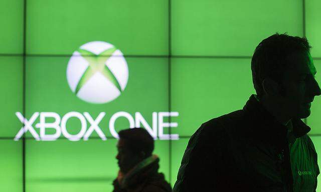 People walk in front of a screen advertising the Xbox One at an event celebrating the console´s midnight launch in New York