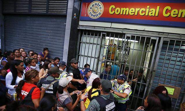 People line up to buy toilet paper and baby diapers as national guards control the access at a supermarket in downtown Caracas