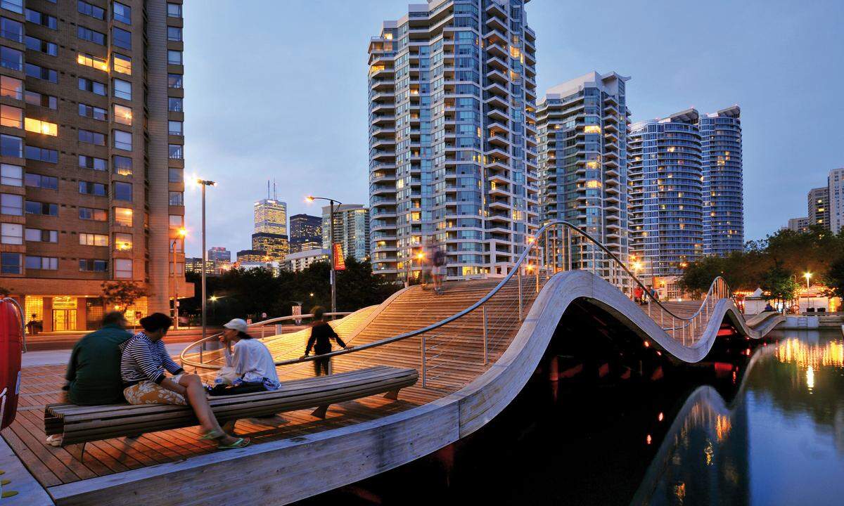 Mit ihren sanften, unregelmäßigen Wellen schließt das "Wavedecks"-Brückenprojekt in Toronto die Lücke zwischen Uferbebauung und dem Wasser des Lake Ontario. Mehrere dieser Brücken sollen im Zuge der Revitalisierung der Uferpromenade entstehen - mit einer Gesamtlänge von dreieinhalb Kilometern. Das vom Büro West 8 Urban Design &amp; Landscape Architecture Ensemble soll Flanierer zum Verweilen einladen - und zum Genießen sowohl des Ausblicks auf die Stadt als auf den See.(© Waterfront Toronto)