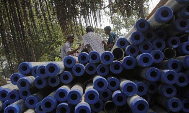 Workers sit on iron pipes before loading them on a truck at an iron and steel market in an industrial area in Mumbai