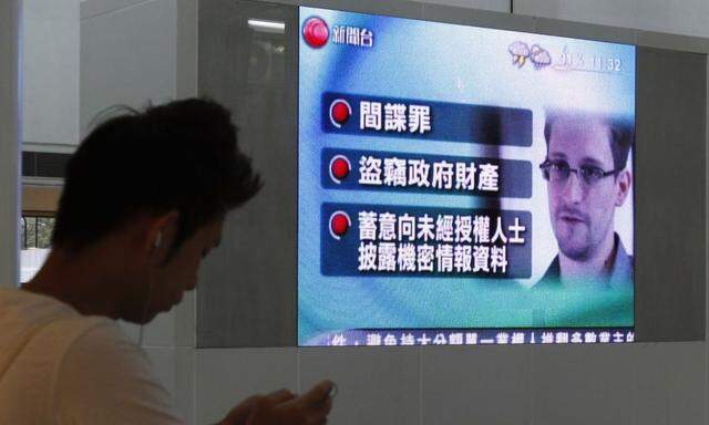 A man checks his phone in front of a monitor broadcasting news on U.S. charges against Snowden, in Hong Kong