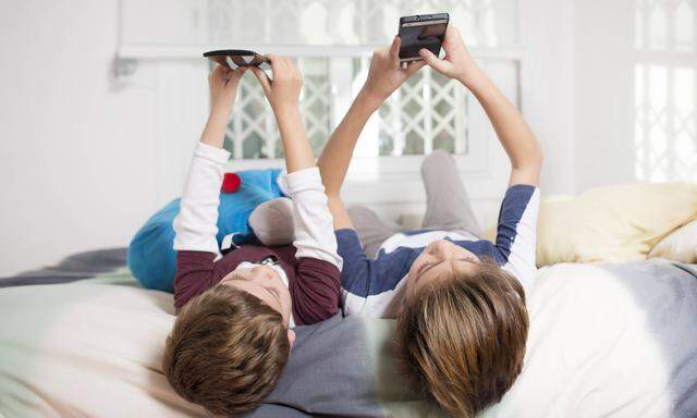 Two boys lying on bed at home using cell phones model released Symbolfoto PUBLICATIONxINxGERxSUIxAUT