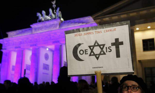 A woman holds up a sign reading ´Coexist´ in front of the Brandenburg Gate prior to vigil for the victims of Paris attacks in Berlin