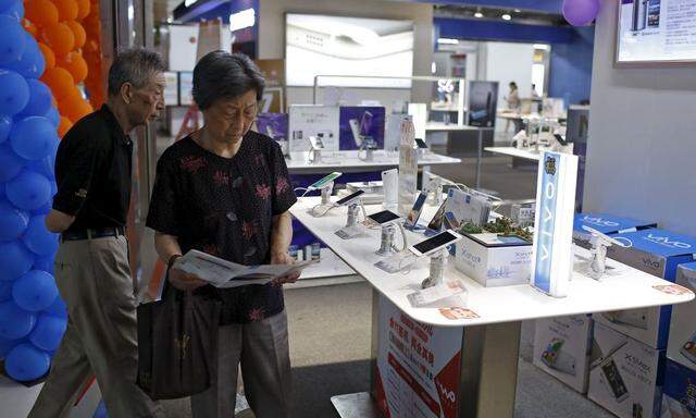 Customers look at mobile phones on display at an electronics market in Shanghai