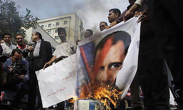 Syrian protesters burn a picture of Syrian President Bashar Assad during a protest in front of the Ar