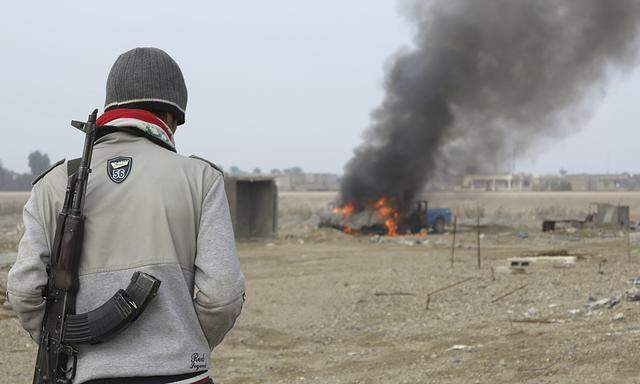 A Sunni Muslim fighter looks at a burning police vehicle during clashes in Ramadi