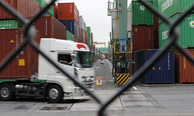 A vehicle travels past containers as seen through a steel fence at a pier in Tokyo