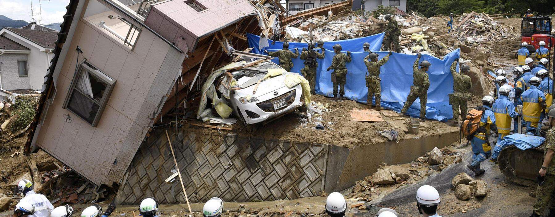 Rescue workers look for missing people in a house damaged by heavy rain in Kumano town