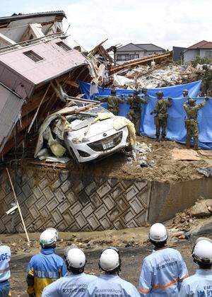 Rescue workers look for missing people in a house damaged by heavy rain in Kumano town