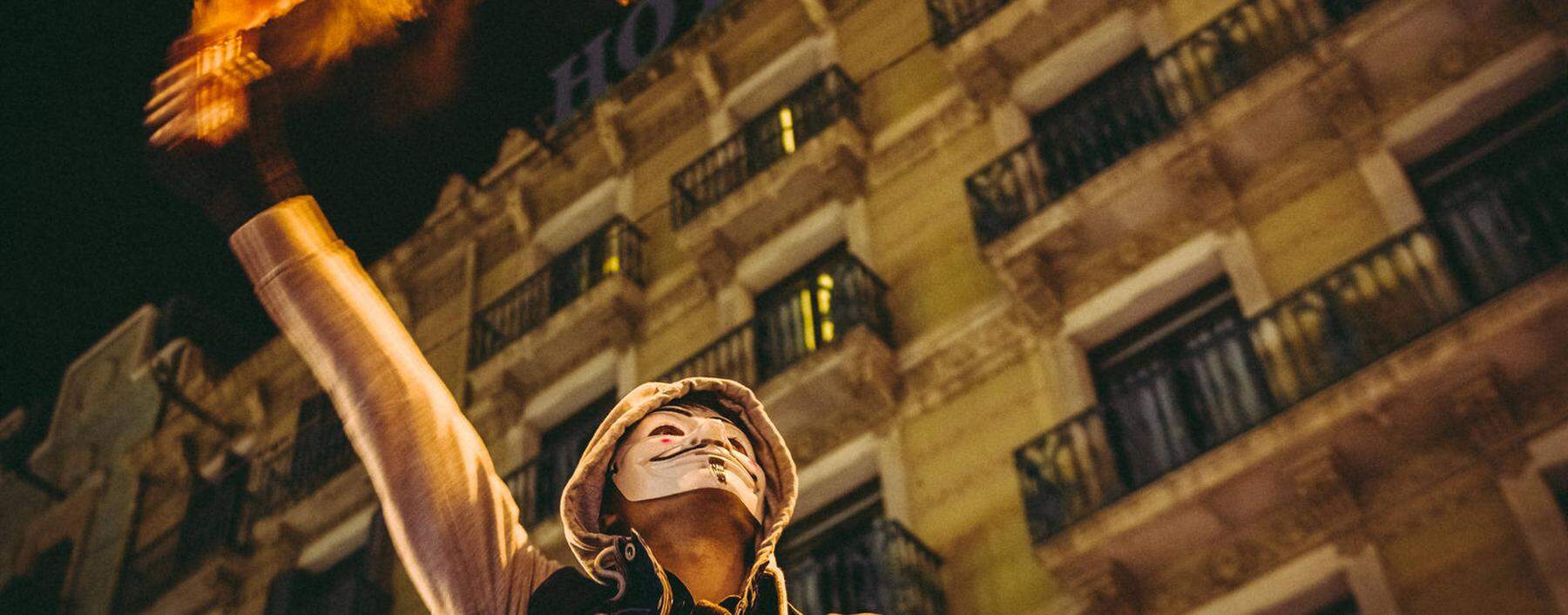 Mit Guy-Fawkes-Maske im Gesicht und Fackel in der Hand: Auch in Katalonien geht es bei den Protesten gegen die Corona-Maßnahmen heiß her. 