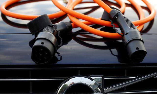 An electric vehicle charging cable is seen on the bonnet of a Volvo hybrid car in this picture illustration