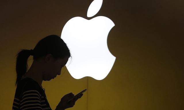 A woman looks at the screen of her mobile phone in front of an Apple logo outside an Apple store in downtown Shanghai