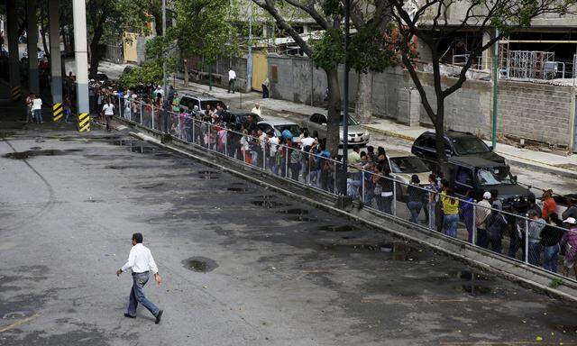 People line up to try to buy basic food items outside a supermarket in Caracas