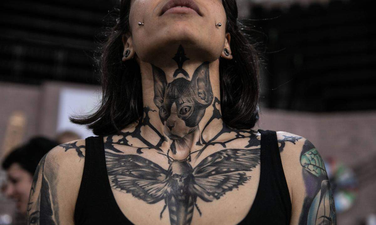 Stolz zeigt eine junge Frau ihr Tattoo, das ihr bis zum Kinn geht, bei der Athener Tattoo-Convention 2019.