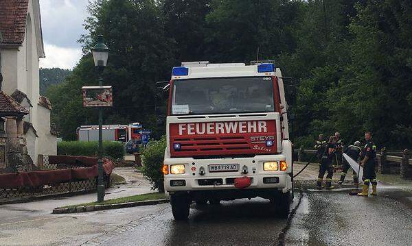 Aufräumarbeiten in Kirchau im Bezirk Neunkirchen in Niederösterreich. Feuerwehr-Einsatzkräfte reinigen die Straße, daneben hängen die Fußbodenteppiche der überfluteten Kirche zum Trocknen.