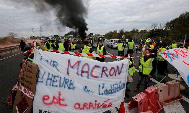 Demonstrators wearing yellow vests, a symbol of a French drivers' protest against higher fuel prices, gather near a pancard critical of president Macron as they block access to the fuel depot in Fos-sur-Mer